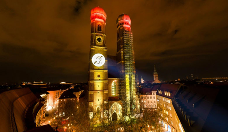 Nachtaufnahme: ein leuchtendes Symbol auf einem Turm der Münchner Frauenkirche. 