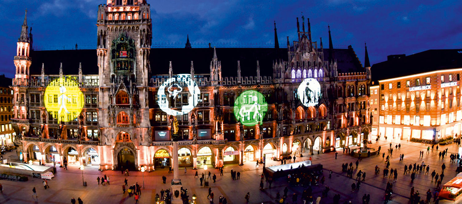 Das Münchner Rathaus bei Nacht. Auf die Fassade sind Symbole für verschiedene Formen von Behinderung projiziert.  